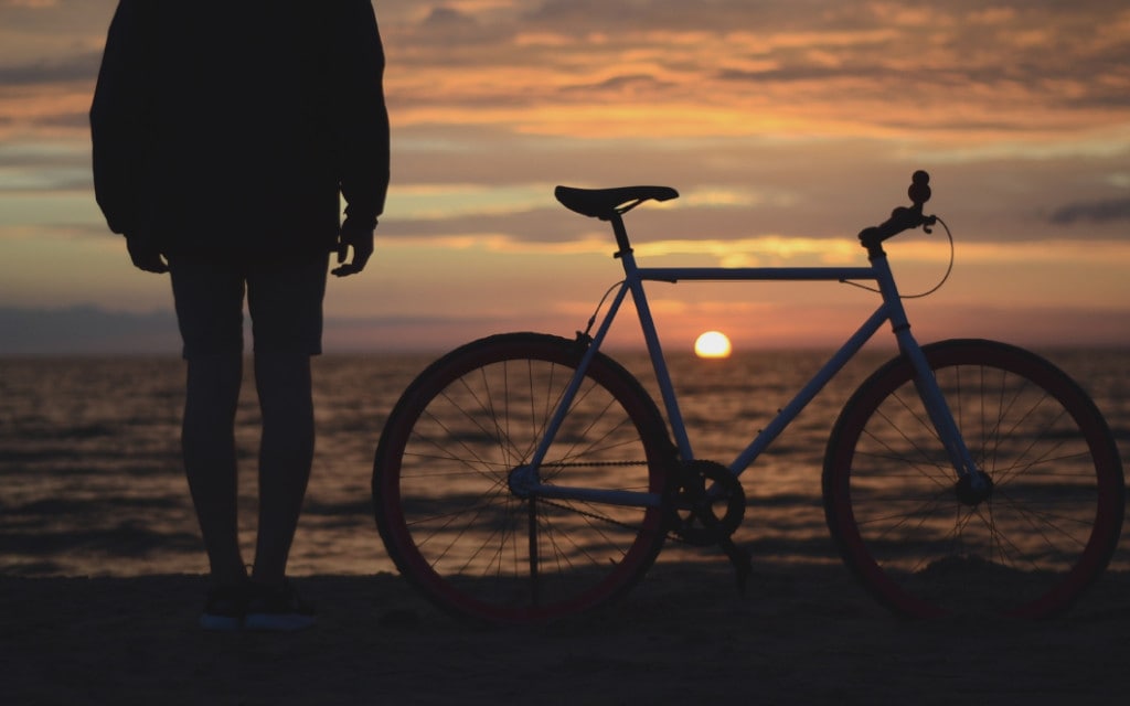 Man next to a bicycle  on the beach enjoying the sunset